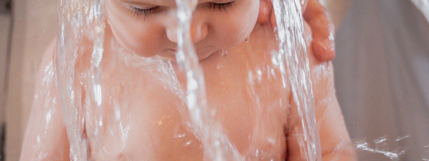Baby bekommt Wasser übner den Kopf beim Babyschwimmen