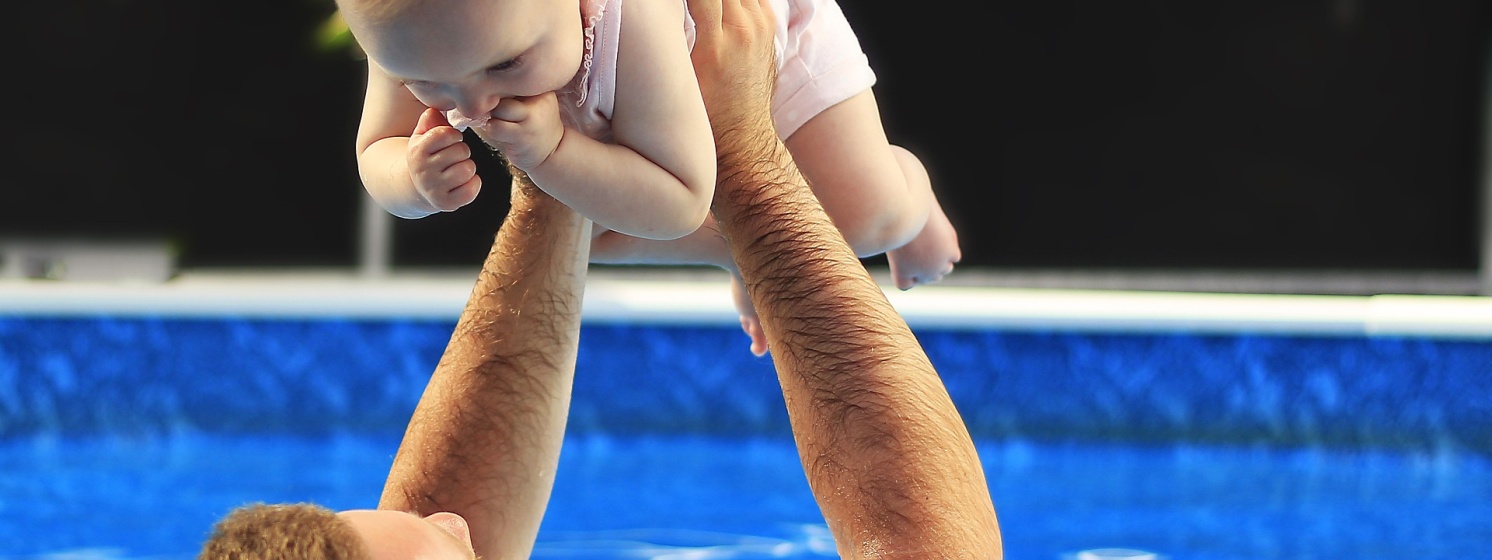 Vater hält Kind beim Babyschwimmen in die Luft